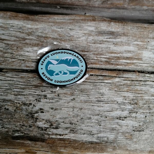 Pieni metallinen ovaalin muotoinen magneetti, ossa on Kevon luonnonpuiston logo. Logossa on naalin kuva