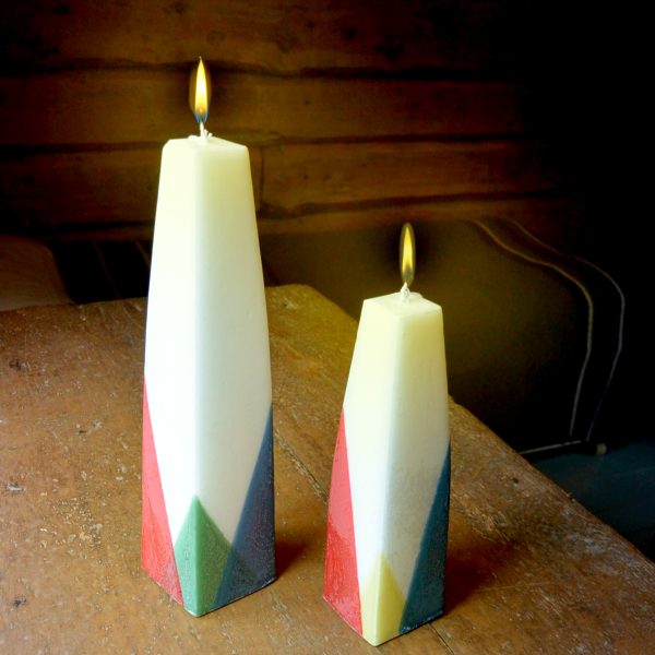 Kynttilätehtaa aurora kynttilät. Valkoisi kantikkaita korkeita kynttilöitä, joidenka alakulmat on kastettu saamenlipun väreillä.