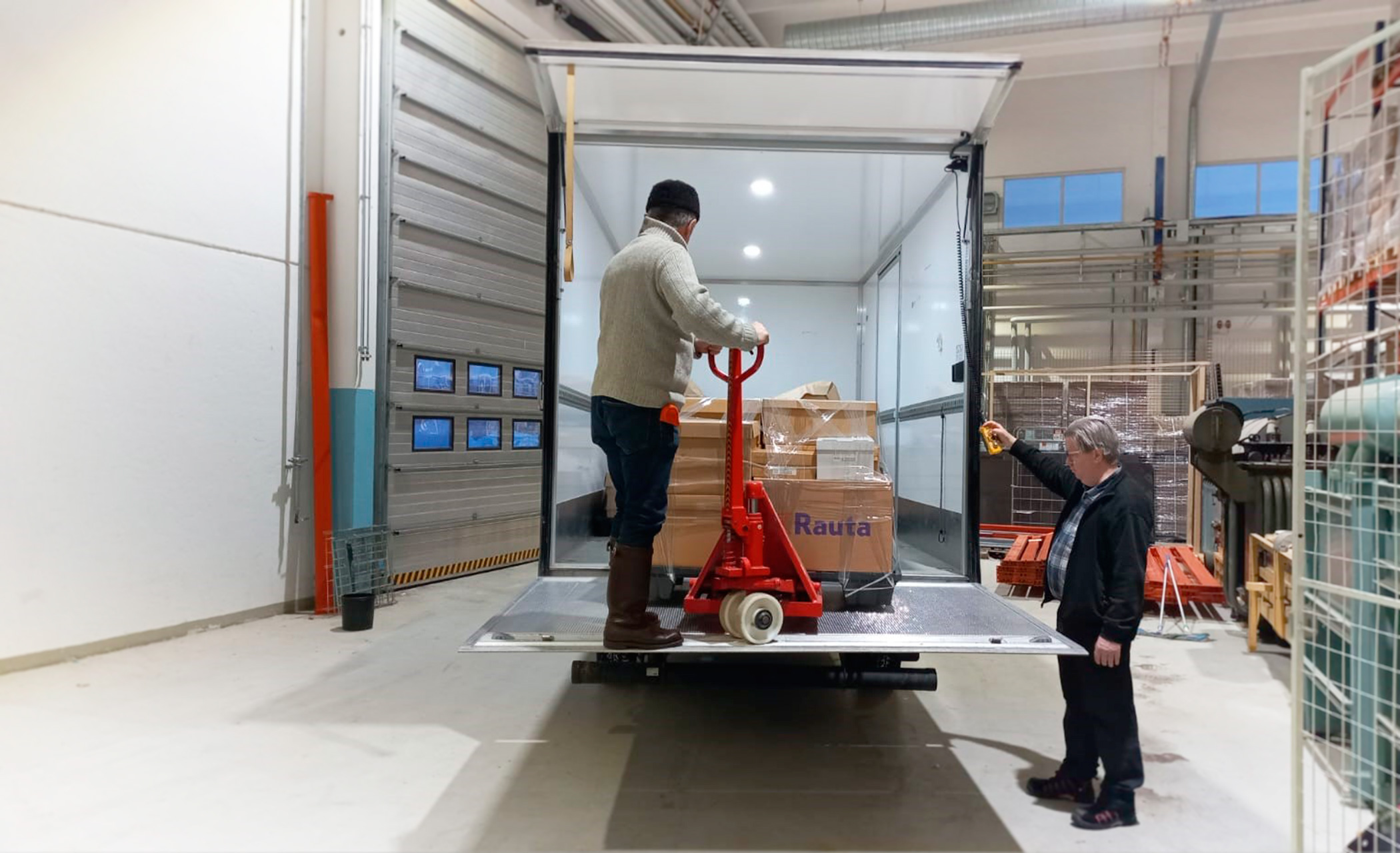 Kuvassa kaksi miestä lastaa autoa varastotiloissa.