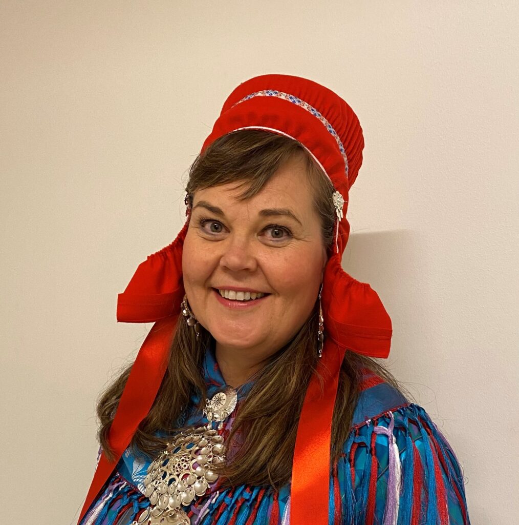 Kuvassa on nainen, jolla on saamenpuku päällä. Nainen hymyilee.